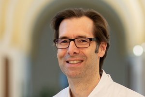 Mann im Arztkittel in warm erleuchtetem Flur mit historischer Gewölbedecke