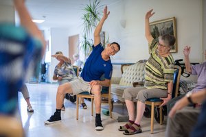 WEin Sportlehrer übt mit betagten Menschen.