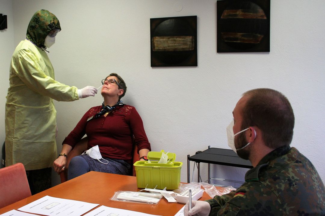 Ein stehender Mann testet mit einem Stäbchen in der Nase bei einer sitzenden Frau, ob sie krank ist.